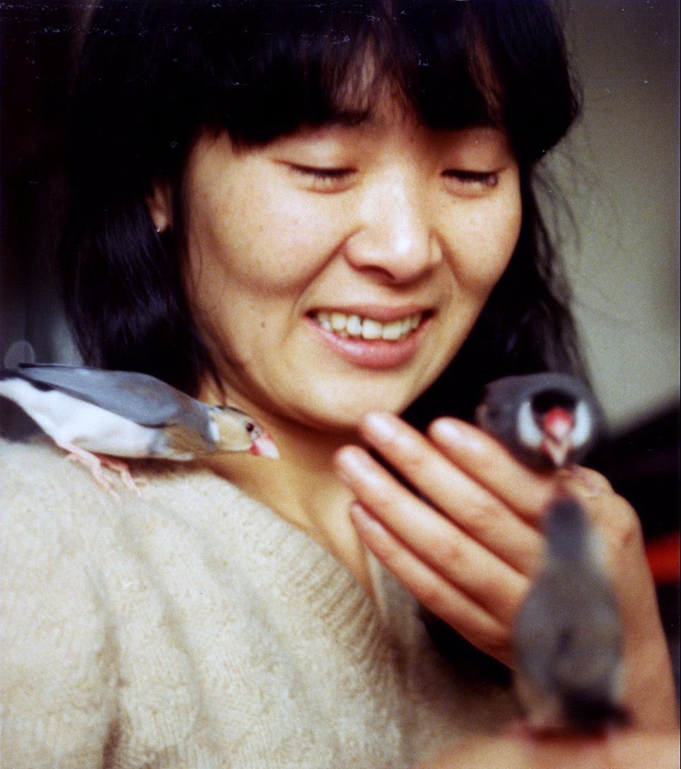 photo portrait of Nazuna Saito, smiling, with a bird in each hand, and one on her shoulder